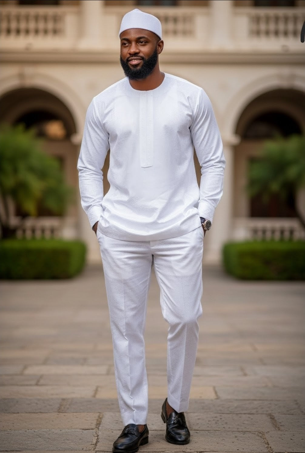 Man in all white Dashiki outfit from Dupsie's African Fashion standing in front of a building with greenery