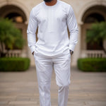 Man in all white Dashiki outfit from Dupsie's African Fashion standing in front of a building with greenery
