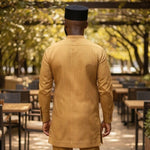 Man in a mustard-colored Dupsie's African traditional outfit walking through an outdoor setting with tables and chairs.