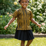 Girl wearing a patterned Kente dashiki top by Dupsie's African fashion and black skirt standing outdoors with greenery in the background