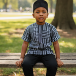 Child sitting on a bench in a park wearing a black and white Kente patterned dashiki shirt and black cap by Dupsie's African fashion