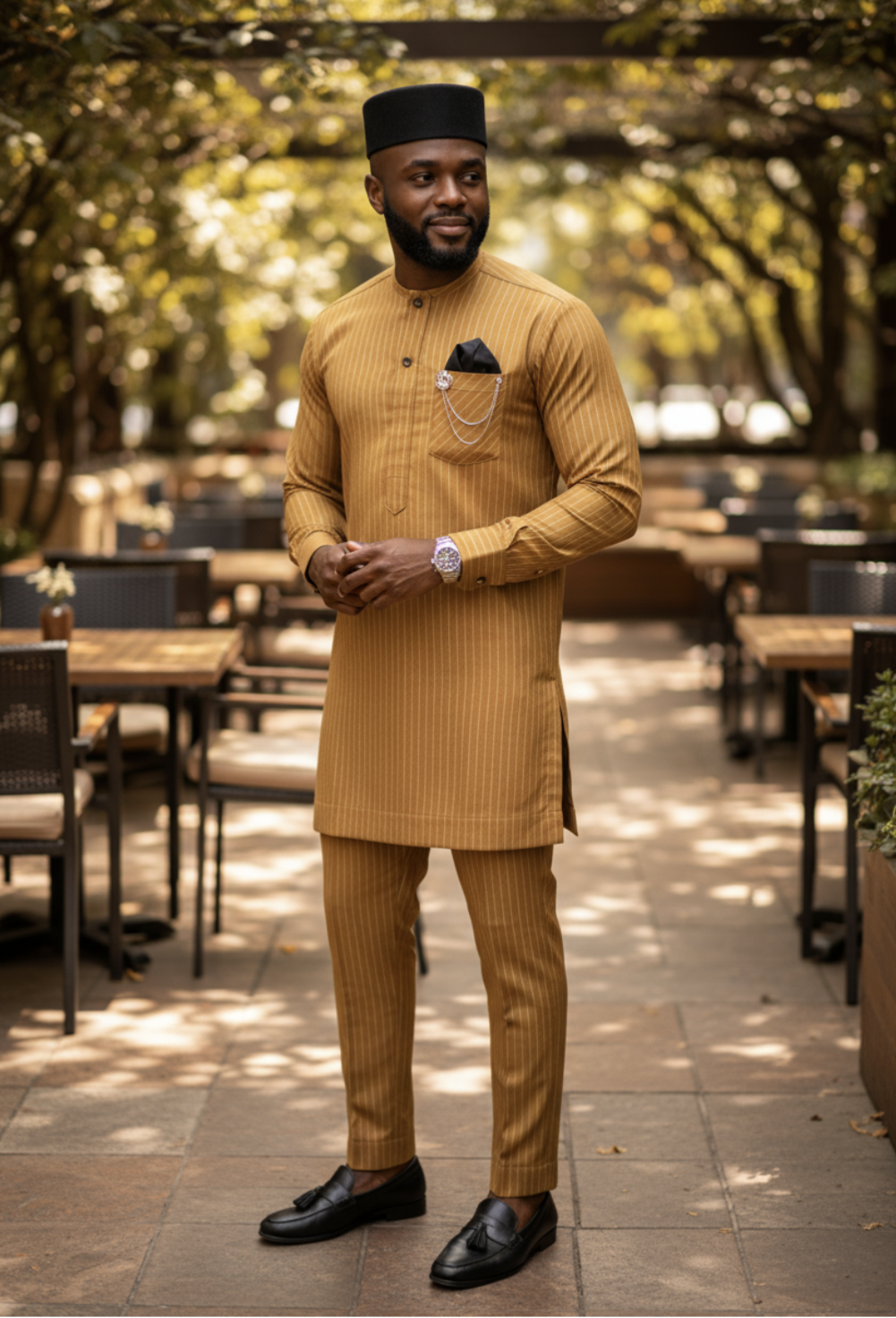 Man in a Gold Dupsie's African traditional outfit standing outdoors with trees and tables in the background