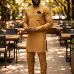 Man in a Gold Dupsie's African traditional outfit standing outdoors with trees and tables in the background
