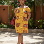 Woman in a yellow patterned dress with red accessories standing outdoors.