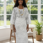 Woman in a white lace dress by Dupsie's with a gold headpiece standing in a bright room with large windows.