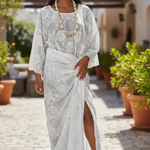 Woman in a white lace dress by Dupsie's African fashion standing outdoors with plants and a building in the background