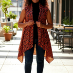 Close-up of lightweight leaf print fabric on burnt-orange African vest shawl; rolled-edge finish