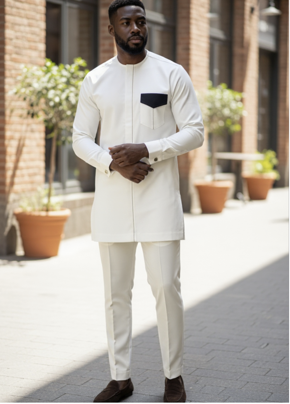 Man wearing a white traditional outfit with a black pocket square in an urban setting.