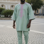 Model wearing a green African Brocade Dashiki top with pink embroidery and matching green drawstring pants; pockets on the top; hat sold separately by Dupsie's African Fashion