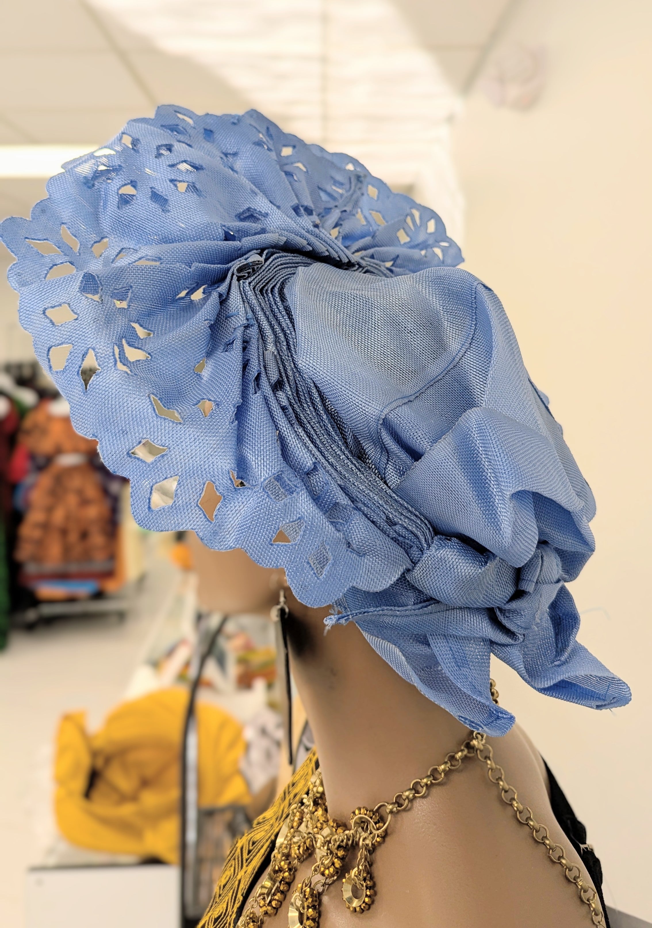 Closeup of fan crown showing rhinestones, glitter, and decorative cutout holes on green Aso Oke.